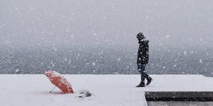 Πεζός περπατά στο χιόνι με ομπρέλα πεσμένη δίπλα του