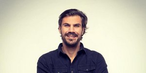 Ο Άκης Πετρετζίκης με σταυρωμένα τα χέρια, φορά μπλε πουκάμισο