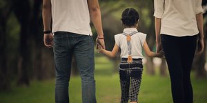 Παιδί περπατά πιασμένο χέρι χέρι με τους γονείς του