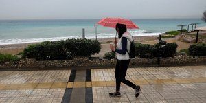 Γυναίκα περπατά με ομπρέλα δίπλα σε θάλασσα