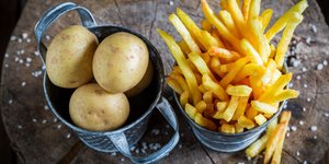 Λαχταριστές τραγανές τηγανητές πατάτες πλάι σε δοχείο με ωμές πατάτες