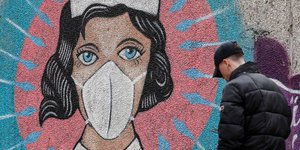 Σκυφτός πολίτης μπροστά σε γκράφιτι που απεικονίζει νοσοκόμα την περίοδο του κορωνοϊού