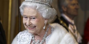 Η Βασίλισσα Ελισάβετ Β' με λευκή γούνα και στέμμα χαμογελά