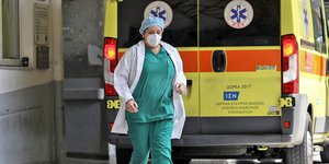 Μια νοσηλεύτρια με μάσκα τρέχει μπροστά από ασθενοφόρο