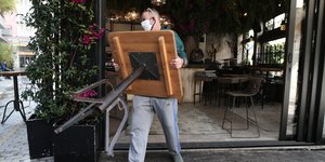 άνδρας με μάσκα για κορωνοϊό κουβαλάει τραπέζι εστίασης