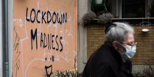 Γυναίκα με μάσκα για τον κορωνοϊό μπροστά από τοίχο που αναγράφει «τρέλα του lockdown» στη Γερμανία