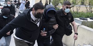 Ο Μένιος Φουρθιώτης με κουκούλα στο πρόσωπο προσάγεται από 2 αστυνομικούς