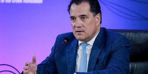 Άδωνις Γεωργιάδης σε καρέκλα με μπλε κοστούμι και μιλάει σε μικρόφωνο