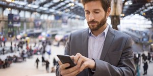 Άνδρας συμβουλεύεται το κινητό του τηλέφωνο σε αεροδρόμιο