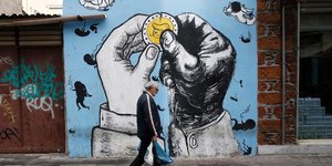 άνδρας περπατά μπροστά από γκράφιτι με χέρια που κρατούν νόμισμα