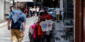 άνδρας με τσάντα περπατάει στην Πλάκα δίπλα από ρούχα