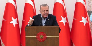 Ο Ρετζέπ Ταγίπ Ερντογάν μιλάει χτυπώντας το χέρι στο βήμα με φόντο τουρκικές σημαίες