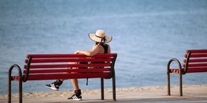 Γυναίκα καθισμένη σε παγκάκι ρεμβάζει στη θάλασσα