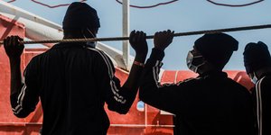 μετανάστες με μάσκες σε πλοίο κοιτάζονται