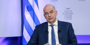 O Νίκος Δένδιας κάθεται με φόντο πίσω του την ελληνική σημασία