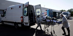 Νοσοκόμοι μεταφέρουν με φορείο ασθενή του κορωνοϊού από ασθενοφόρο