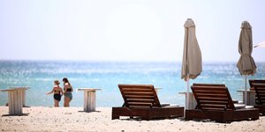 Παραλία θάλασσα με ξαπλώστρες και δυο γυναίκες με μαγιό στο φόντο