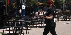 σερβιτόρα με δίσκο στο χέρι περπατά σε πεζόδρομο έξω από μαγαζί