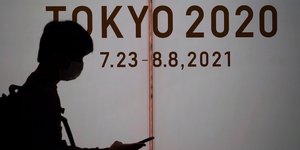 Ανθρωπος στη σκιά με κινητό στο χέρι περνάει από σήμα με Ολυμπιακούς Αγώνες Τόκιο