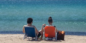 άνδρας και γυναίκα κάθονται σε καρέκλες στην παραλία με άμμο