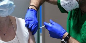 νοσηλευτής με πράσινη στολή κάνει εμβόλιο κατά κορωνοϊού σε γυναίκα