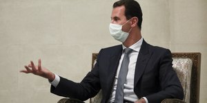 Ο Μπασάρ αλ-Άσαντ με μάσκα και κοστούμι σε καρέκλα