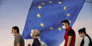 κόσμος με μάσκες μπροστά από ευρωπαϊκή σημαία