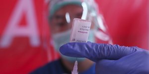 εμβόλιο στα χέρια νοσηλευτή με μπλε γάντια και διαφανή μάσκα μπροστά από κόκκινος τοίχος