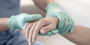 νοσηλευτής με πράσινα γάντια σε χέρι ασθενούς σε νοσοκομείο