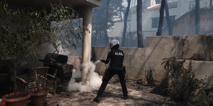 Ανδρας της ΔΙΑΣ μέσα σε αυλή σπιτιού ρίχνει νερό για να σβήσει τη φωτιά