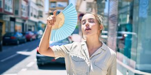 κοπέλα περπατά στο δρόμο και κάνει αέρα με βεντάλια λόγω ζέστης