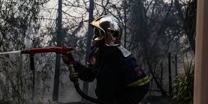 πυροσβέστης με μάνικα και κράνος σβήνει φωτιά