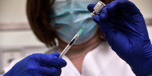 υγειονομικός με μπλε γάντια κρατά εμβόλιο