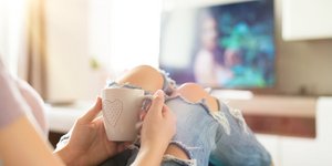 Γυναίκα με καφέ στα χέρια βλέπει τηλεόραση