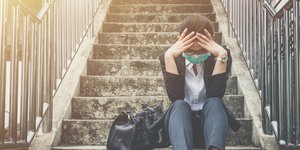 γυναίκα με μάσκα κάθεται σε σκαλιά σκεπτική