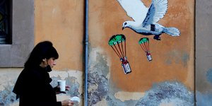 γυναίκα με μάσκα στην Ιταλία περνά μπροστά από γκράφιτι με περιστέρι