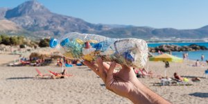 χέρι κρατά πλαστικό μπουκάλι σε ελληνική παραλία