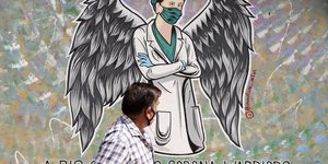 Άνδρας με μάσκα περνά μπροστά από γκράφιτι αγγέλου γιατρού