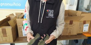 Εθελόντρια από το «Μαζί για το Παιδί» κρατά ένα ζευγάρι παπούτσια από την εταιρεία TOMS, τα οποία διανεμήθηκαν σε παιδιά που έχουν ανάγκη 