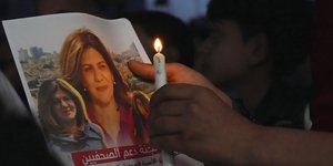 Παλαιστίνιος κρατά ένα αναμμένο κερί και μια φωτογραφία της δολοφονημένης δημοσιογράφου του Al Jazeera, Shireen Abu Akleh,