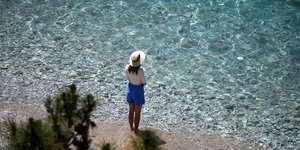 κοπέλα με καπέλο όρθια στη θάλασσα με καλό καιρό