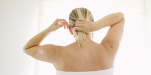 Γυναίκα τυλιγμένη σε λευκή πετσέτα στέκεται στο μπάνιο και δένει τα βρεγμένα μαλλιά της