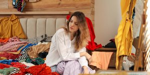 Νεαρή γυναίκα περιτριγυρισμένη από διάφορα ρούχα σε ακατάστατο δωμάτιο