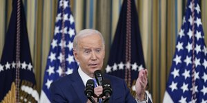 O Τζο Μπάιντεν μιλά στο μικρόφωνο με φόντο Αμερικανικές σημαίες