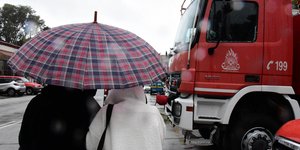 Ατομα με ομπρέλα μπροστά από όχημα της πυροσβεστικής