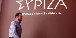 O Νίκος Παππάς περπατάει μπροστά από το σήμα του ΣΥΡΙΖΑ