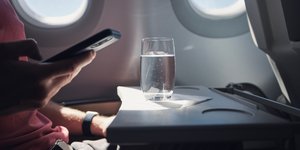 Άνδρας σε αεροπλάνο κρατά κινητό και μπροστά του έχει ένα ποτήρι νερό