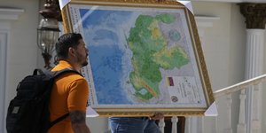 Άνδρας μεταφέρει τον νέο χάρτη της Βενεζουέλας με την επικράτεια Essequibo, μια μεγάλη έκταση γης που διαχειρίζεται και ελέγχεται από τη Γουιάνα αλλά διεκδικείται από τη Βενεζουέλα