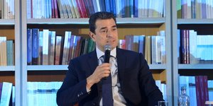 O Kώστας Σκρέκας μιλάει με φόντο βιβλία