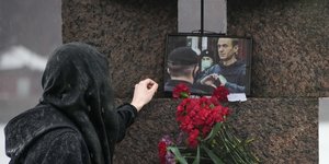 Μια γυναίκα αγγίζει μια φωτογραφία του Αλεξέι Ναβάλνι μετά την κατάθεση λουλουδιών για να του αποτίσει τον τελευταίο φόρο τιμής στο μνημείο για τα θύματα της πολιτικής καταπίεσης στην Αγία Πετρούπολη